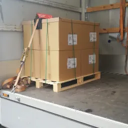 Cztery kartony na palecie zabezpieczone pasami transportowymi wewnątrz przestrzeni ładunkowej samochodu dostawczego.