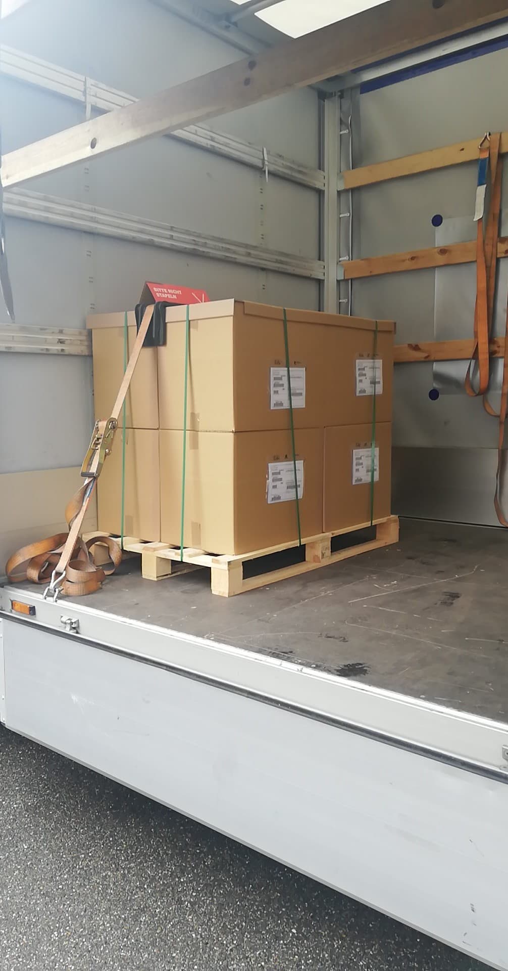 Cztery kartony na palecie zabezpieczone pasami transportowymi wewnątrz przestrzeni ładunkowej samochodu dostawczego.