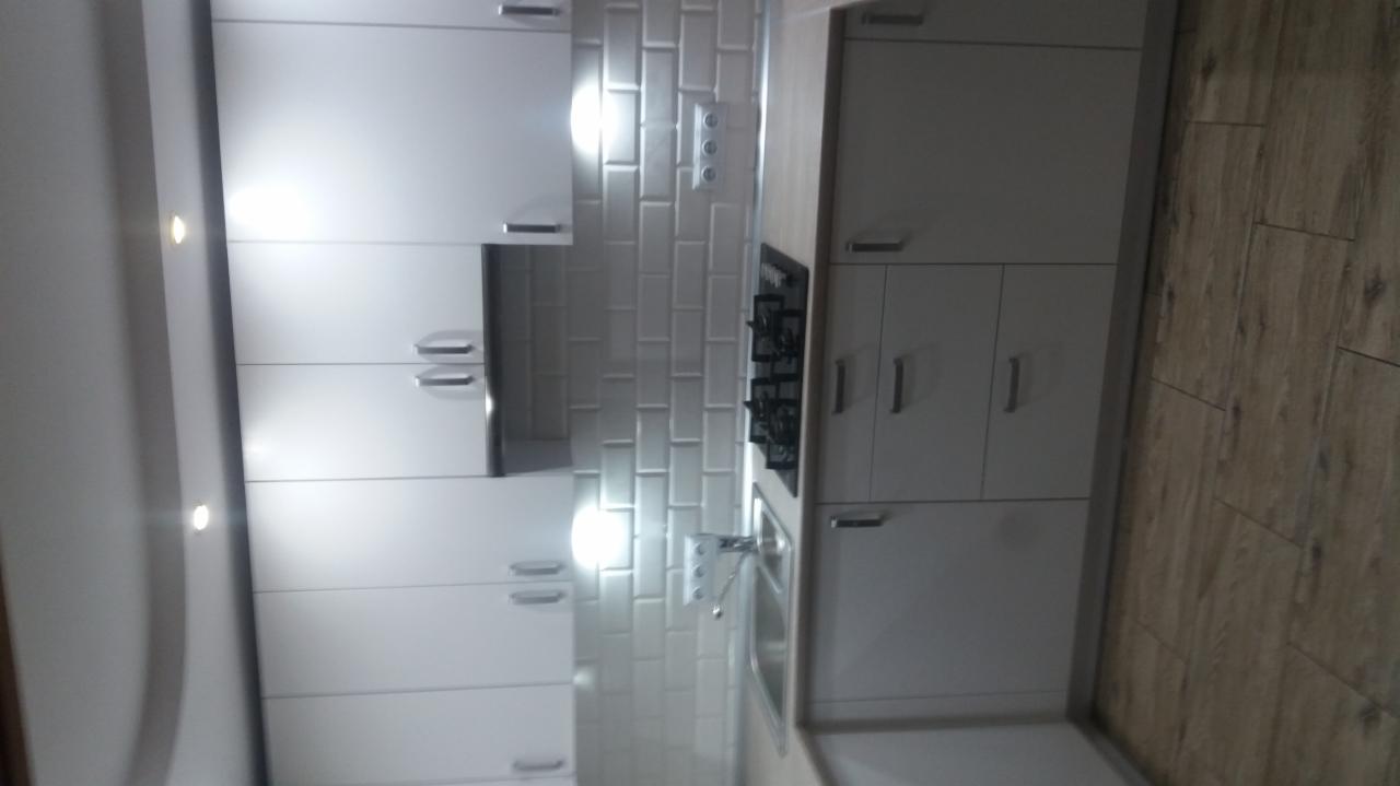 Nowoczesna, biała kuchnia z płytkami typu metro na ścianie, drewnopodobną podłogą i wbudowanym oświetleniem punktowym.