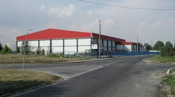 Hala magazynowa z czerwonym dachem w Michałowicach, widok z drogi, szara nawierzchnia, błękitne niebo z chmurami w tle.