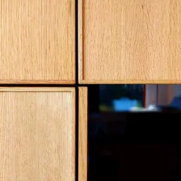 Detaliczne ujęcie czterech drewnianych frontów szafki z widocznym usłojeniem, z ciemnym, nieostrym tłem wnętrza.
