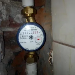 Licznik gazu GSD8 z widocznym wskazaniem 00000505 m3, zamontowany na rurach w pomieszczeniu z fragmentami ceglanej ściany i białych płytek.