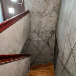 Betonowe ściany klatki schodowej z dekoracyjnymi, geometrycznymi liniami, drewniane schody i poręcze, widok z góry.