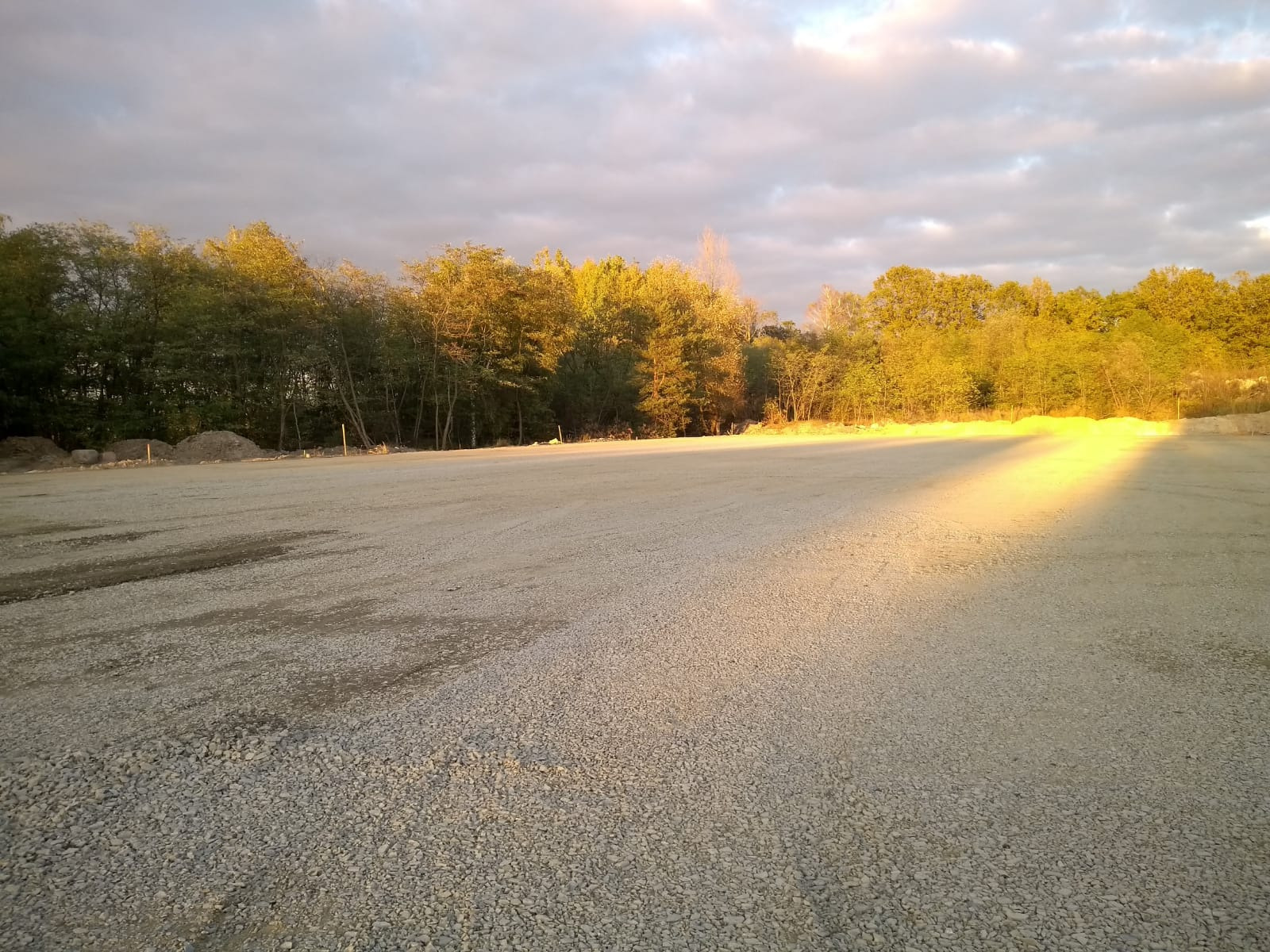 Przygotowany teren pod budowę magazynu, wyrównany żwir, w tle drzewa oświetlone zachodzącym słońcem.