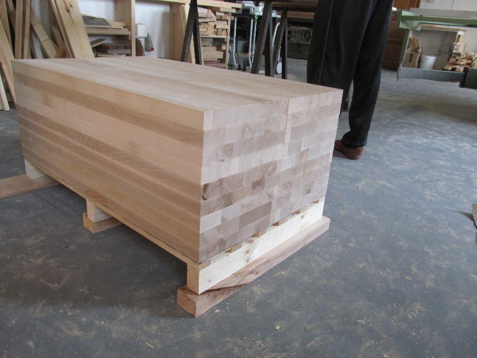 Blok z klejonego drewna na drewnianych podkładkach, przygotowany do obróbki na schody, widoczne warstwy drewna o różnym odcieniu.