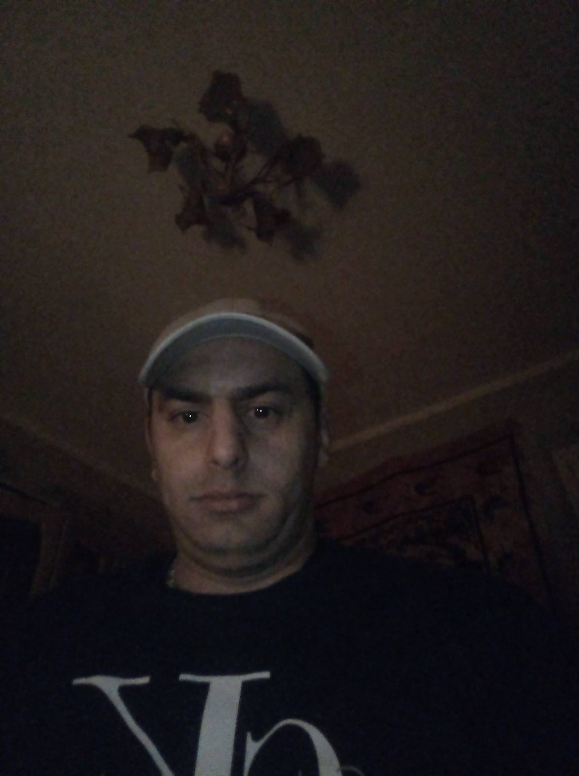 Portret mężczyzny w czarnej koszulce i beżowej czapce z daszkiem, z lampą w tle, w słabym oświetleniu.