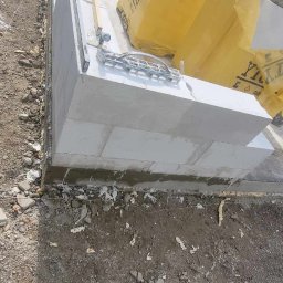 ESPANIOL-BUD - Budowa fundamentów z bloczków Ytong, widoczne narzędzia murarskie i paczki bloczków w żółtej folii.