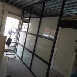 ESPANIOL-BUD - Montaż wewnętrznej ścianki działowej z czarną ramą i wypełnieniem z mlecznego szkła, widoczna drabina rozstawiona przy oknie.