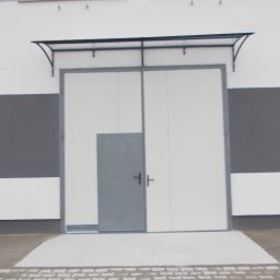 Metaloplastyka , konstrukcje stalowe , spawanie, ślusarka - Biała brama dwuskrzydłowa z szarym obramowaniem i wbudowanymi drzwiami, zamontowana w szaro-białej elewacji budynku z oknami i małym daszkiem. Przed nią kostka brukowa.