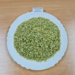 Rozdrobniony chmiel zwyczajny (szyszka cięta) na białym talerzu, leżącym na drewnianym stole, z małą etykietą z nazwą rośliny.