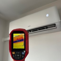 MIKOLI.pl Piotr Kowalski - Pomiar termowizyjny białego klimatyzatora ściennego, z ekranem czerwonego termowizora pokazującym temperatury 23.5°C i 10.2°C.