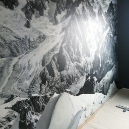 Andrii Korytchuk GLOBAL-REM - Fototapeta z motywem górskim w odcieniach szarości, częściowo przykryta folią ochronną na podłodze podczas montażu, widoczny fragment ściany pomalowanej na ciemny kolor.