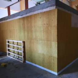 Ocieplenie ścian wełną mineralną w surowym stanie, widoczna drabina i paleta drewniana, etap prac wykończeniowych.