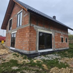 ST SITO PROJECT SPÓŁKA Z OGRANICZONĄ ODPOWIEDZIALNOŚCIĄ - Surowy budynek z czerwonej cegły z czarnymi ramami okiennymi i ciemnym dachem, w trakcie budowy, widok z zewnątrz w pochmurny dzień.