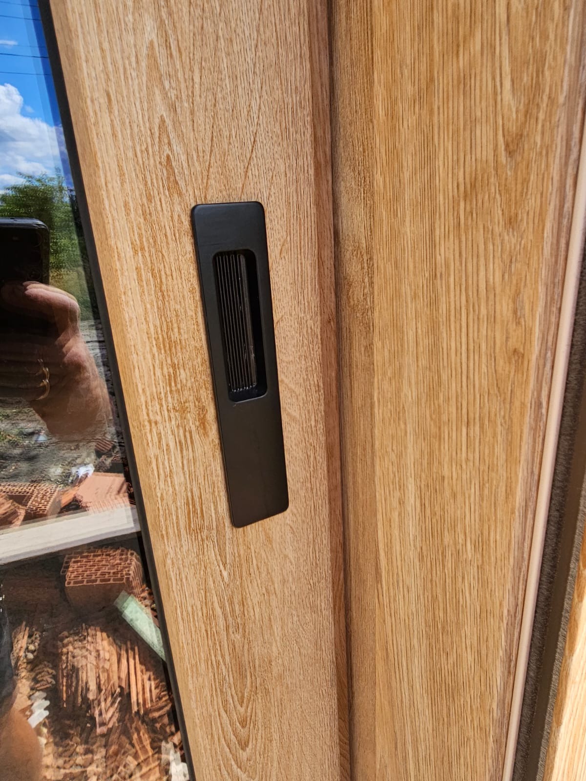 Drewnopodobne drzwi przesuwne z czarnym, wpuszczanym uchwytem. Widoczne detale wykończenia i refleksy w szybie. Ujęcie z bliska, podkreślające fakturę.