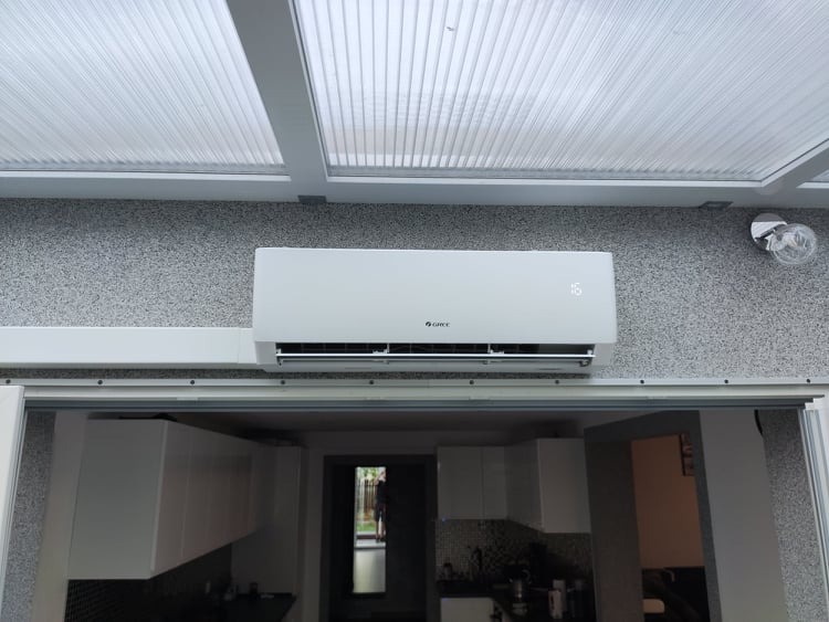 Biały klimatyzator marki Gree zamontowany na ścianie z szarą, ziarnistą fakturą w pomieszczeniu w Przecławiu, widoczne oświetlenie sufitowe i fragment przeszklonego dachu.