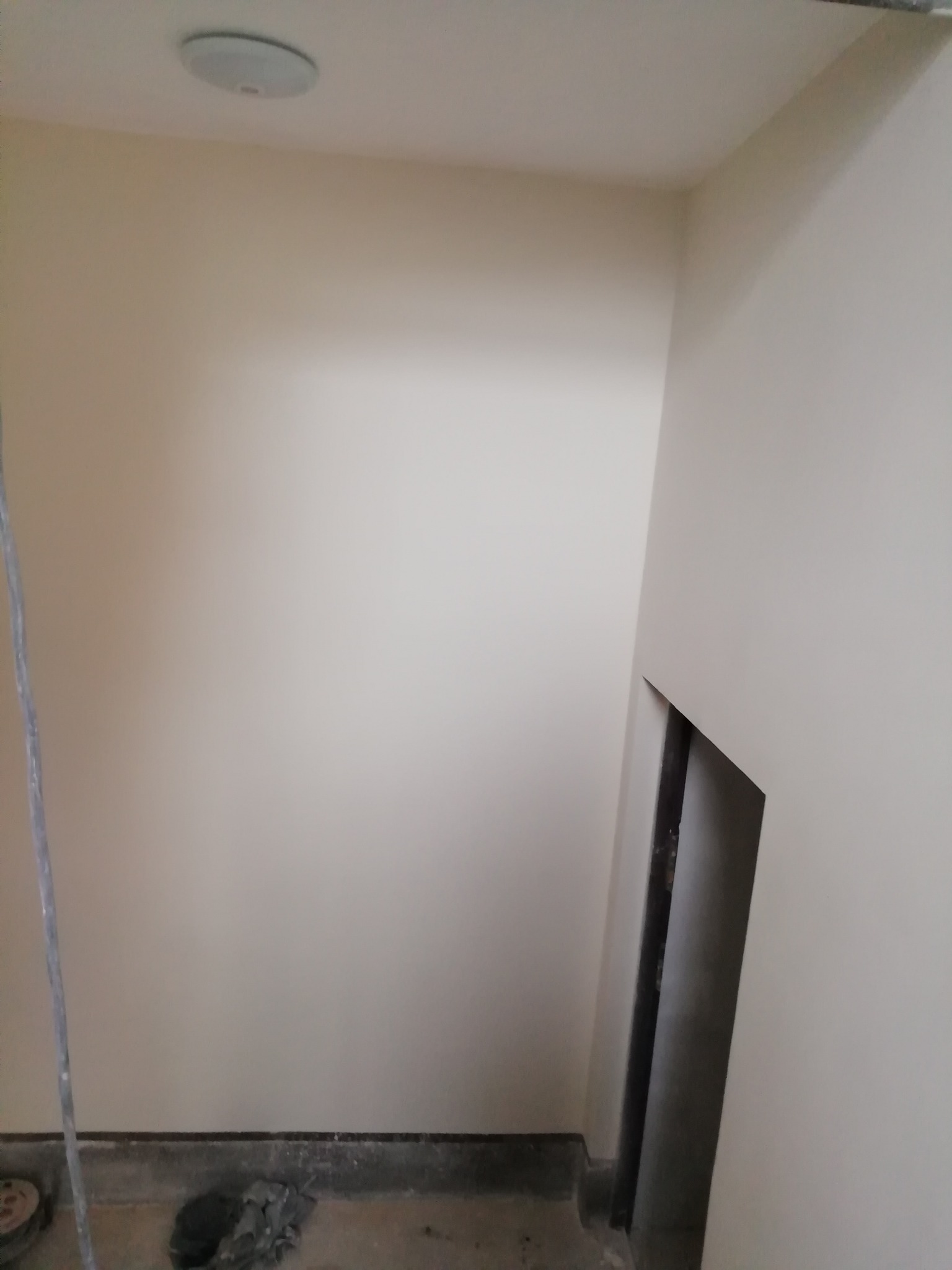 Świeżo pomalowane ściany w odcieniu beżu, widoczny fragment futryny drzwiowej i sufit z okrągłą lampą, na podłodze resztki po pracy.