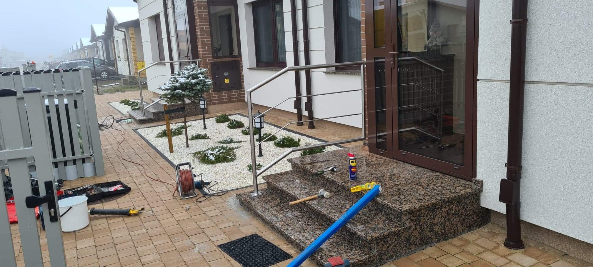 Montaż poręczy ze stali nierdzewnej przy wejściu do domu w Koziegłowach, widoczne narzędzia i materiały budowlane na stopniach.