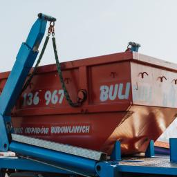 Wywóz gruzu Warszawa - Czerwony kontener na odpady budowlane z numerem telefonu, podnoszony przez niebieski dźwig na tle jasnego nieba i częściowo widocznych drzew.