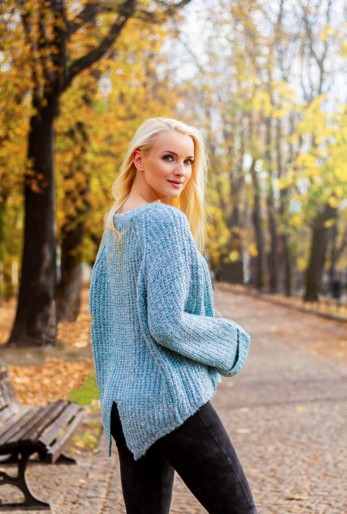 Blondwłosa kobieta w niebieskim swetrze spogląda przez ramię w jesiennym parku.