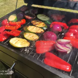 Grillowane warzywa: czerwona papryka, cebula i cukinia na ruszcie, z widocznymi śladami grillowania i delikatnym dymem.