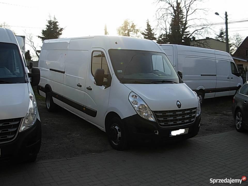 Białe busy Renault Master zaparkowane na brukowanym placu, widoczne z przodu, jeden z lekko otwartymi drzwiami kierowcy.