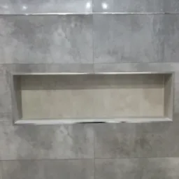 Szare płytki imitujące beton z wnęką wykończoną listwą aluminiową w łazience.