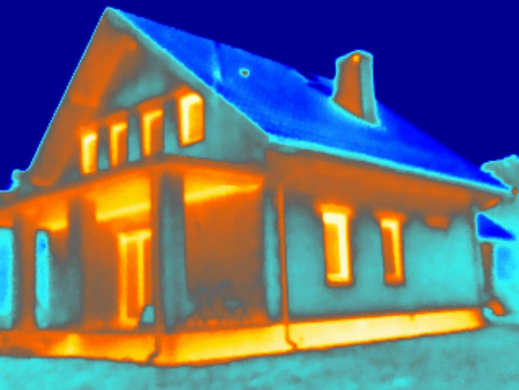 Termowizyjne zdjęcie domu jednorodzinnego, ukazujące straty ciepła przez ściany, okna i dach. Kolorystyka od niebieskiego (zimne) do żółto-pomarańczowego (ciepłe).