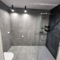 PRO-FACH - Nowoczesna łazienka w odcieniach szarości z kabiną prysznicową typu walk-in i podwieszaną toaletą, oświetlona dwoma punktowymi lampami sufitowymi.