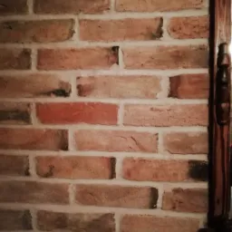 Fragment ceglanej ściany w odcieniach czerwieni i brązu, z widoczną drewnianą kolumną po prawej stronie, tworzącą element dekoracyjny.