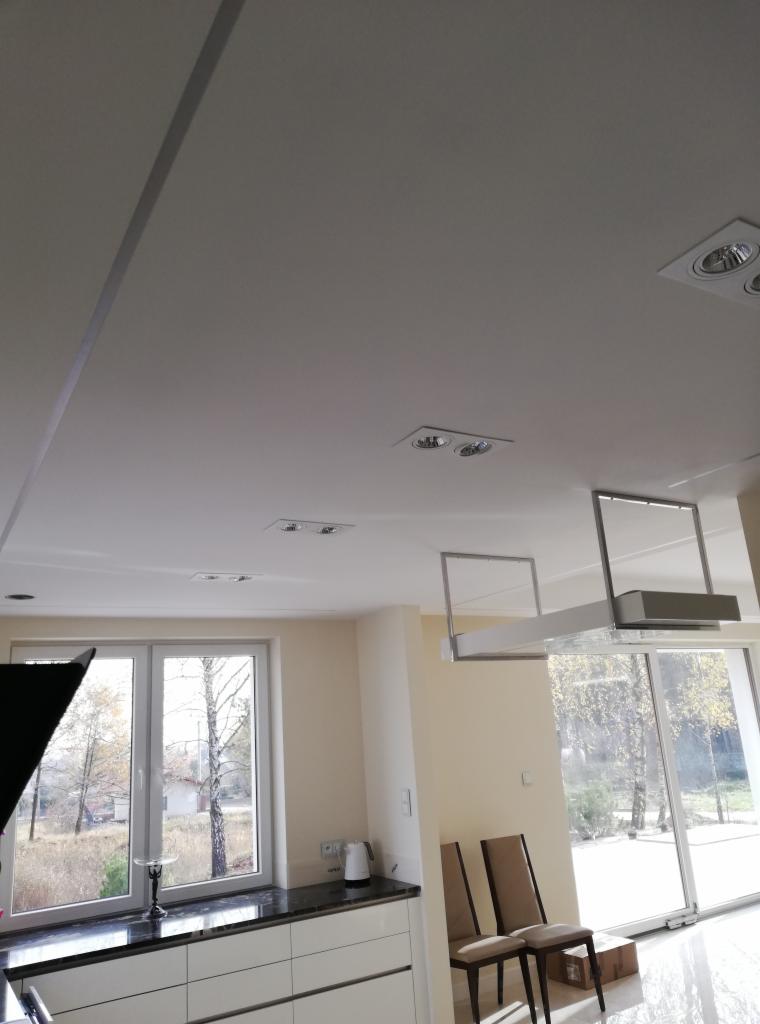 Biały sufit z zamontowanymi punktowymi lampami w nowoczesnej kuchni z widokiem na zewnątrz przez duże okno.