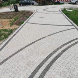 MARBRUK - Nowoczesny chodnik z jasnoszarej kostki brukowej z dekoracyjnymi wstawkami z ciemniejszej kostki, tworzącymi łuki i linie, prowadzący do ulicy z zaparkowanymi samochodami i koszem na śmieci.