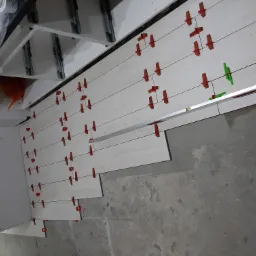 Układanie jasnych, drewnopodobnych płytek na podłodze z użyciem poziomicy i czerwonych krzyżyków dystansowych, widoczny fragment surowej ściany i instalacji pod sufitem.