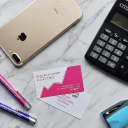 Złoty smartfon, kalkulator Citizen, dwie wizytówki i dwa długopisy z nazwą 'Biuro Rachunkowe Liczydło' oraz niebieski zszywacz na marmurowym tle.