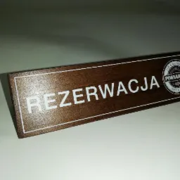 Tabliczka z napisem 'Rezerwacja' i logo 'Piwiarnia Beer & Grill' na brązowym tle, wykonana z drewna.