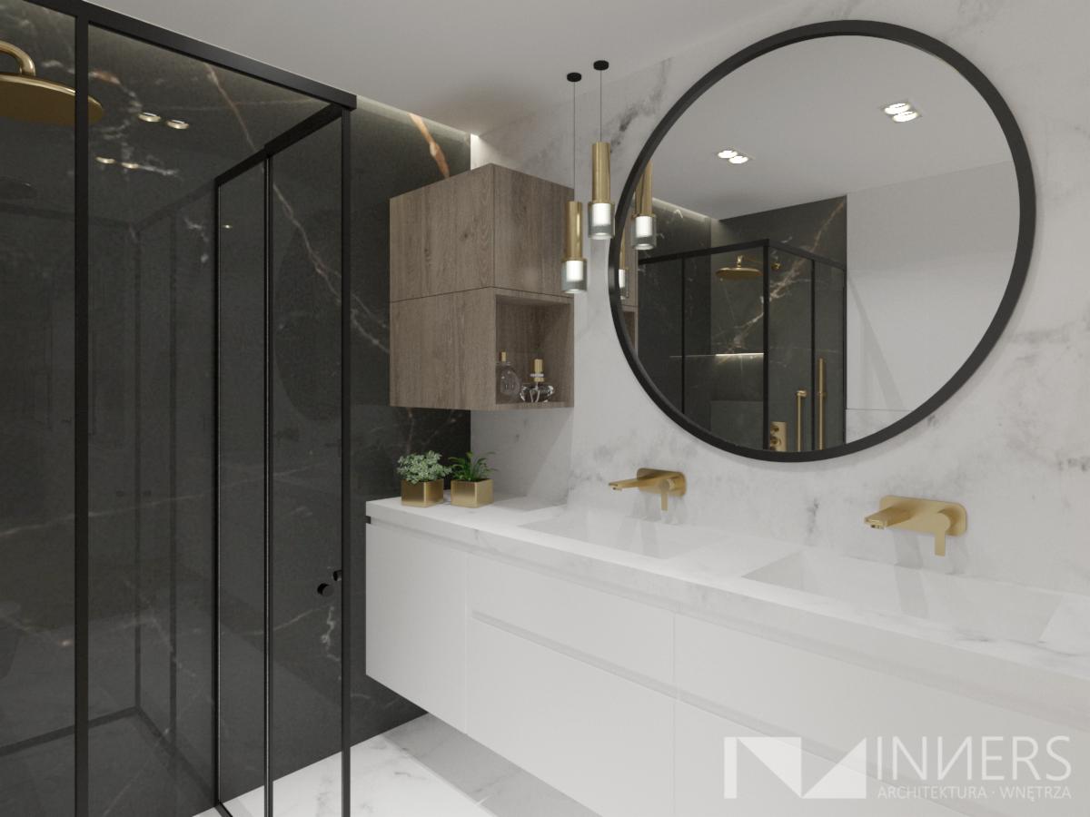 Nowoczesna łazienka z czarną kabiną prysznicową, marmurowymi ścianami, okrągłym lustrem w czarnej ramie, białą szafką z dwoma umywalkami i złotą armaturą oraz wiszącą szafką z drewnianymi frontami.