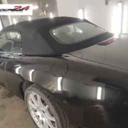 Czarny kabriolet Jaguar z czarnym dachem, widoczny z boku, po polerowaniu lakieru, z refleksami światła w warsztacie.
