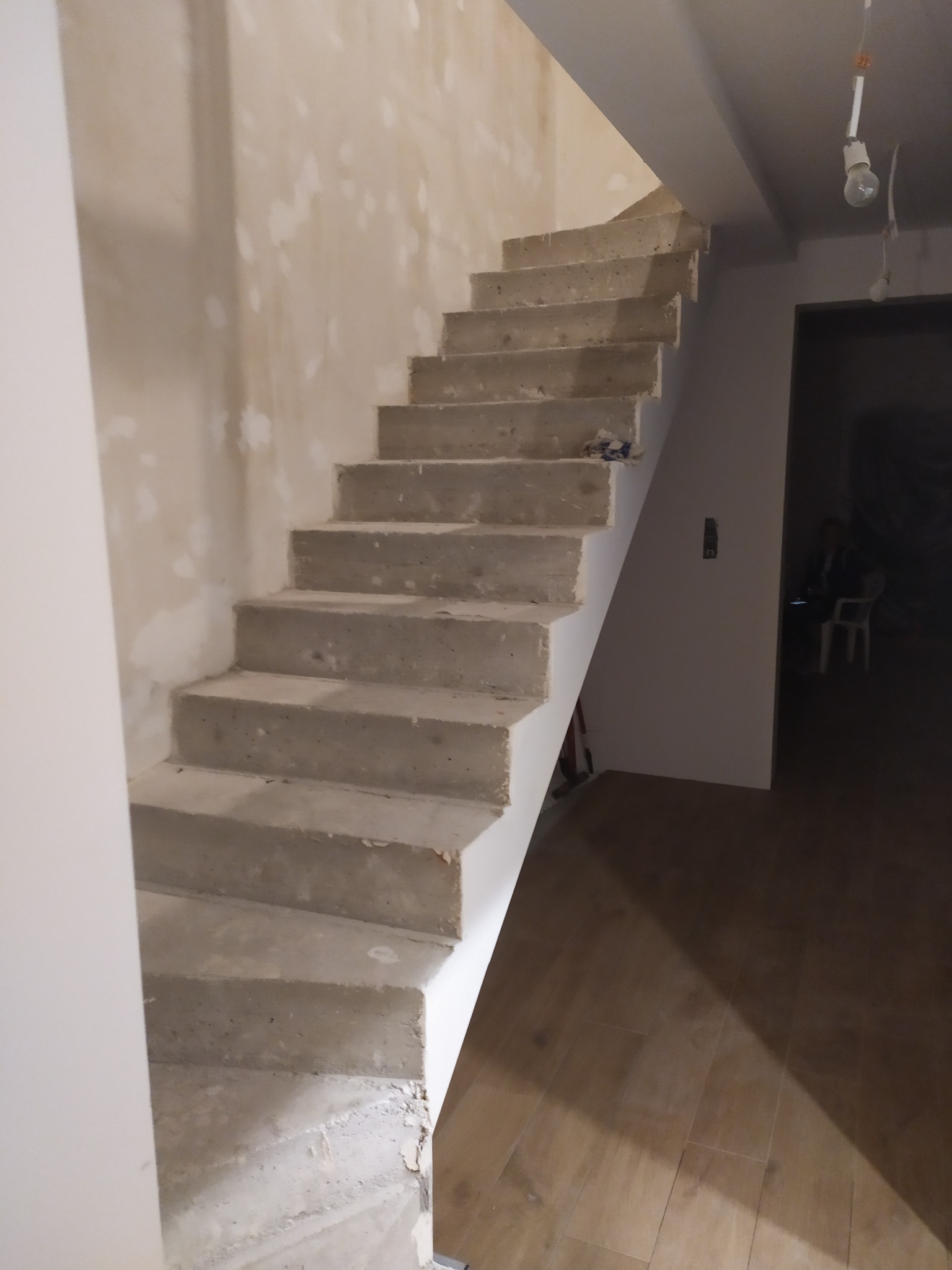 Surowe betonowe schody w trakcie budowy, widoczne niedoskonałości i ślady zaprawy, z fragmentem podłogi wyłożonej panelami imitującymi drewno.