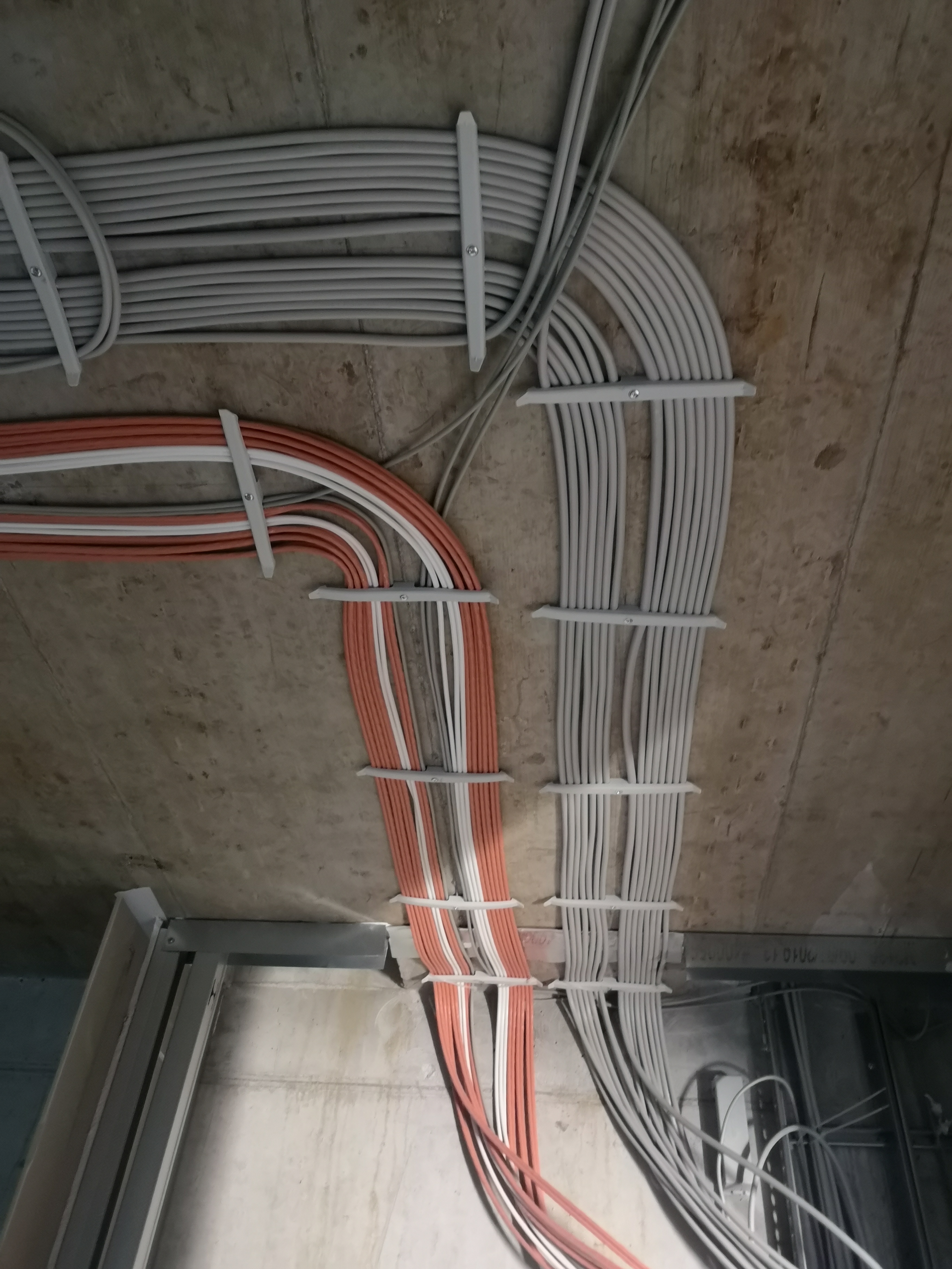 Instalacja elektryczna w nowym budynku w Gorzowie Wielkopolskim: uporządkowane kable w kolorze szarym i pomarańczowo-białym, przymocowane do sufitu za pomocą specjalnych uchwytów.