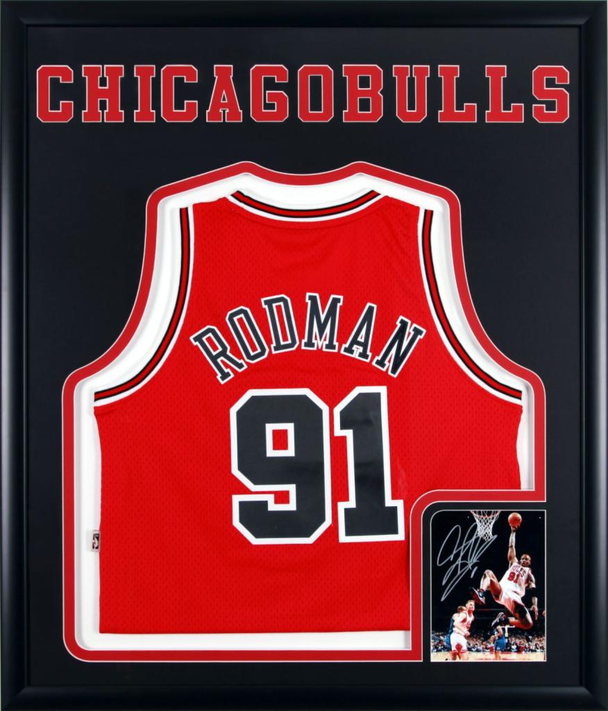 Oprawiona w ramę koszulka Chicago Bulls z nazwiskiem Rodman i numerem 91, obok zdjęcie z autografem Rodmana podczas meczu.