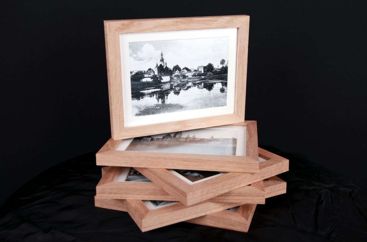 Stos drewnianych ramek na zdjęcia z czarno-białymi fotografiami krajobrazu, ułożonych kaskadowo na czarnym tle.