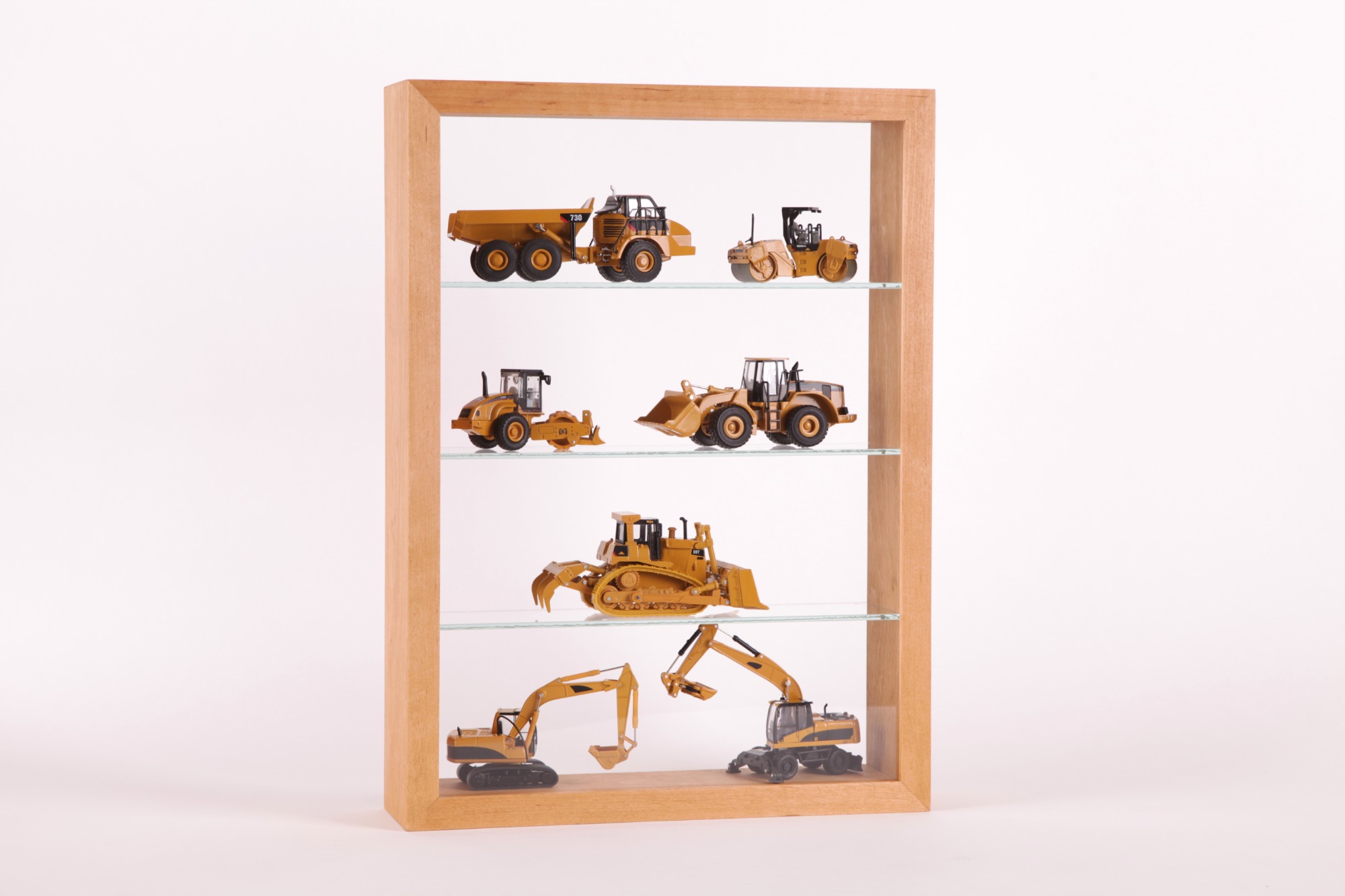 Kolekcja modeli maszyn budowlanych Caterpillar w drewnianej gablocie z szklanymi półkami, obejmująca wywrotkę, walec, spychacz, ładowarki i koparki.