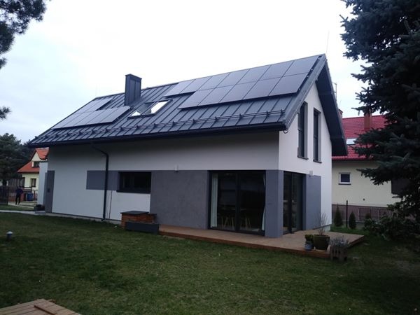 Nowoczesny dom jednorodzinny z panelami fotowoltaicznymi na dachu, widok z ogrodu w pochmurny dzień.