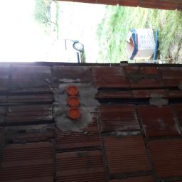 ELPRO Usługi Elektryczne Dawid Olszewski - Fragment ściany z cegły dziurawki z trzema pomarańczowymi puszkami elektrycznymi zamontowanymi w szarym cemencie, widoczne peszle instalacyjne, w tle trawa i samochód