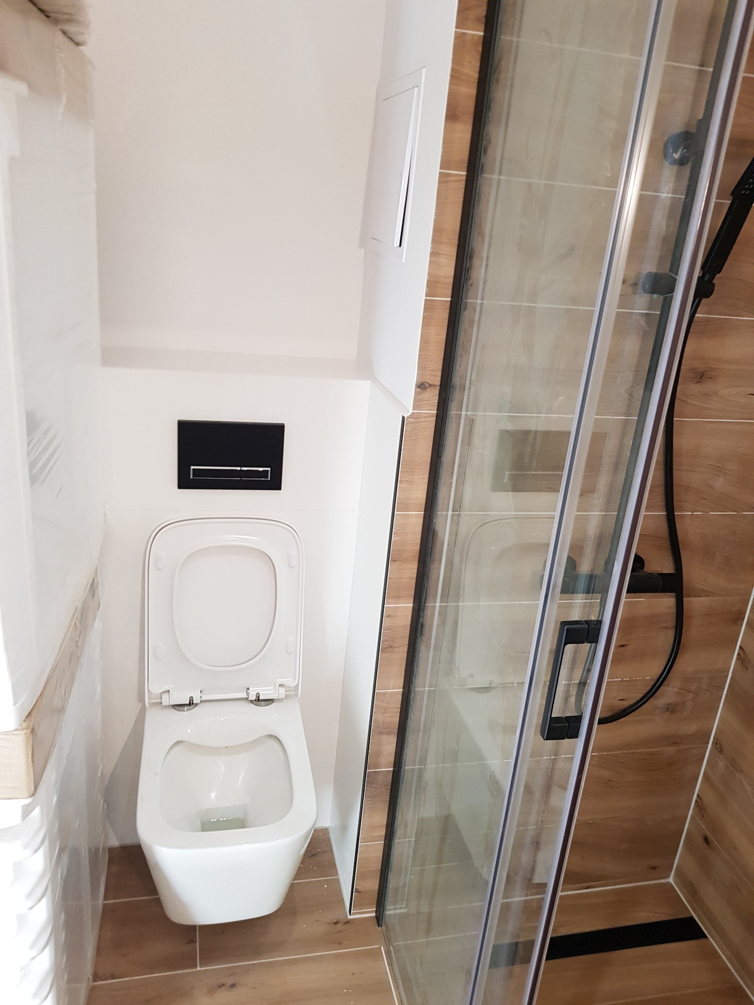 Nowoczesna, wykończona łazienka w Ostrołęce z kabiną prysznicową ze szkła i białym sedesem wiszącym z czarnym przyciskiem spłukującym.