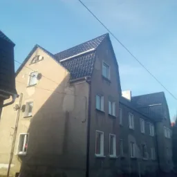 Budynek wielorodzinny z nowym, błyszczącym, ciemnym dachem z dachówki ceramicznej, widoczny z dołu, z przewodami elektrycznymi na pierwszym planie.