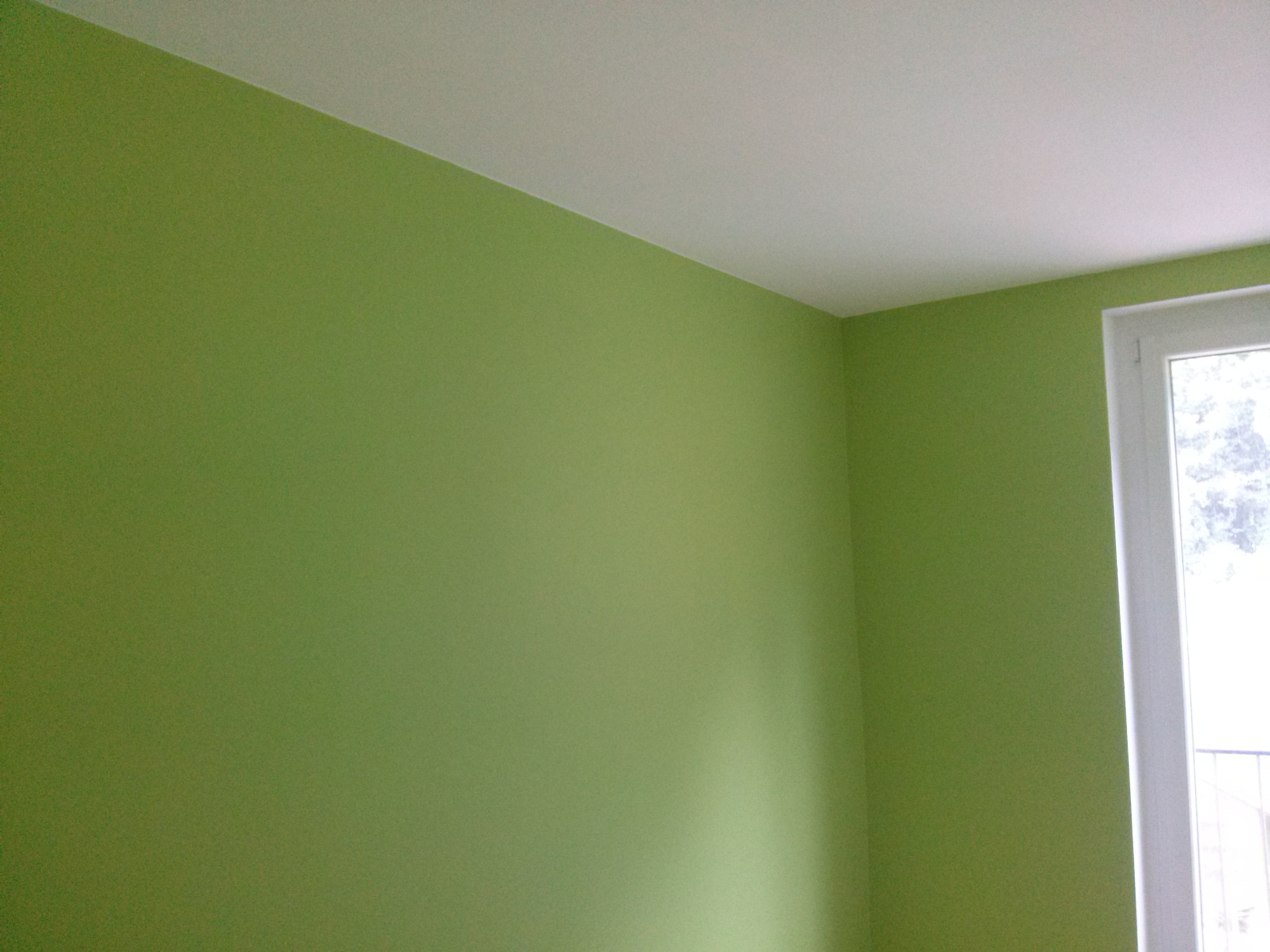 Świeżo pomalowane na zielono ściany w rogu pokoju, z białym sufitem i ramą okienną.