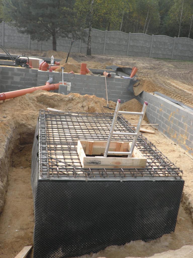 Fundament z hydroizolacją, zbrojony stalą, przygotowany pod budowę, widoczna drabina i elementy instalacji rurowej w wykopie