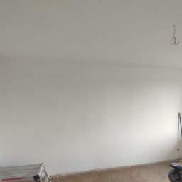 hiro - Świeżo pomalowane na biało ściany pokoju z parkietem, widoczna drabina malarska, odkurzacz przemysłowy i hak w suficie.