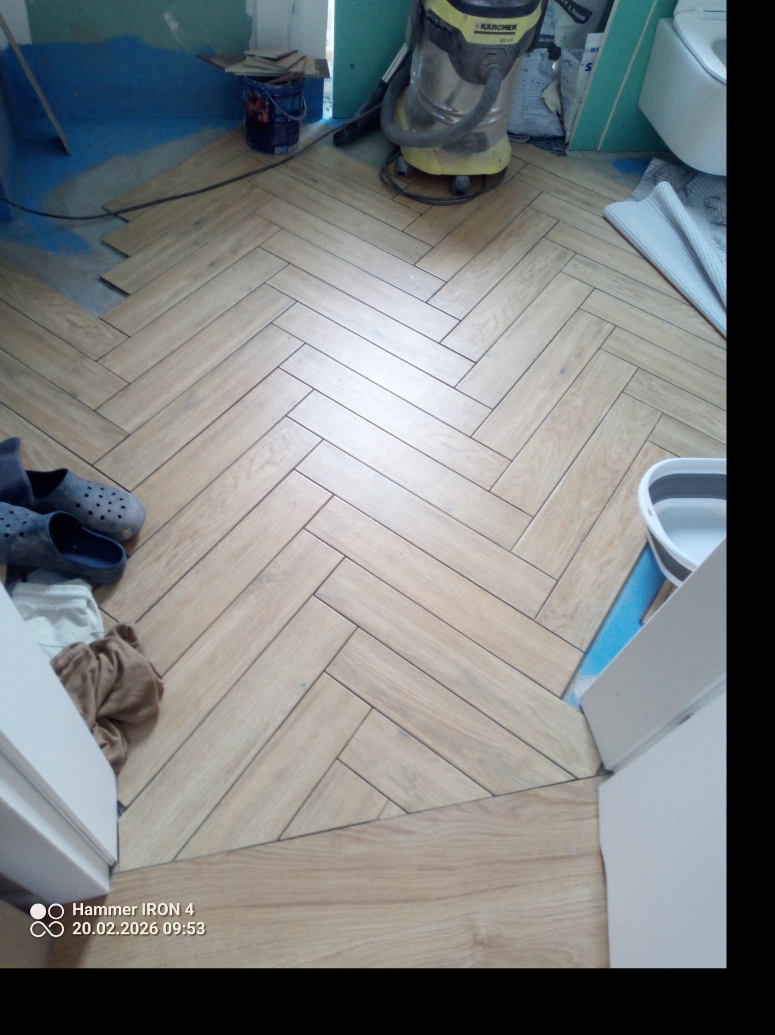 Ułożona parkietowa podłoga w jodełkę w trakcie prac wykończeniowych, widoczny odkurzacz przemysłowy i akcesoria malarskie. Jasne drewno, wzór jodełki.